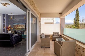 A balcony with wicker furniture, a flat-screen TV, and a stone wall. - Nightingale Villa & Suites- Jiannis Villa (Corfu)