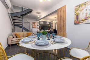 A dining area with a round table set for four, surrounded by yellow chairs, a sofa, and a staircase. - Nightingale Villa & Suites- Jiannis Villa (Corfu)