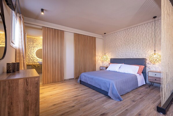 A modern bedroom with a large bed, wooden floor, and a sliding door leading to a bathroom.