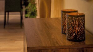 Une table en bois, agrémentée de deux chandeliers décoratifs, un miroir et une vue sur un coin cuisine.