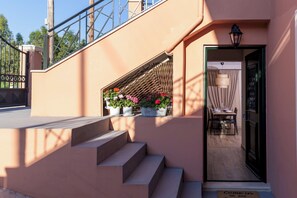 A hotel entrance with a set of steps leading to a door, a small outdoor seating area with potted plants, and a visible doormat with a welcoming message.