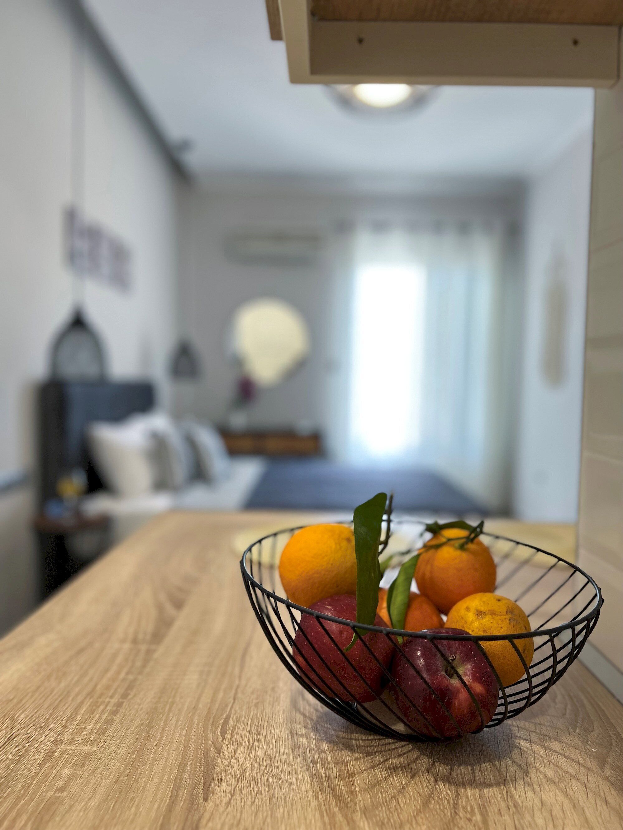 Een schaal fruit op een houten tafel in een hotelkamer, met een bed en nachtkastje op de achtergrond.