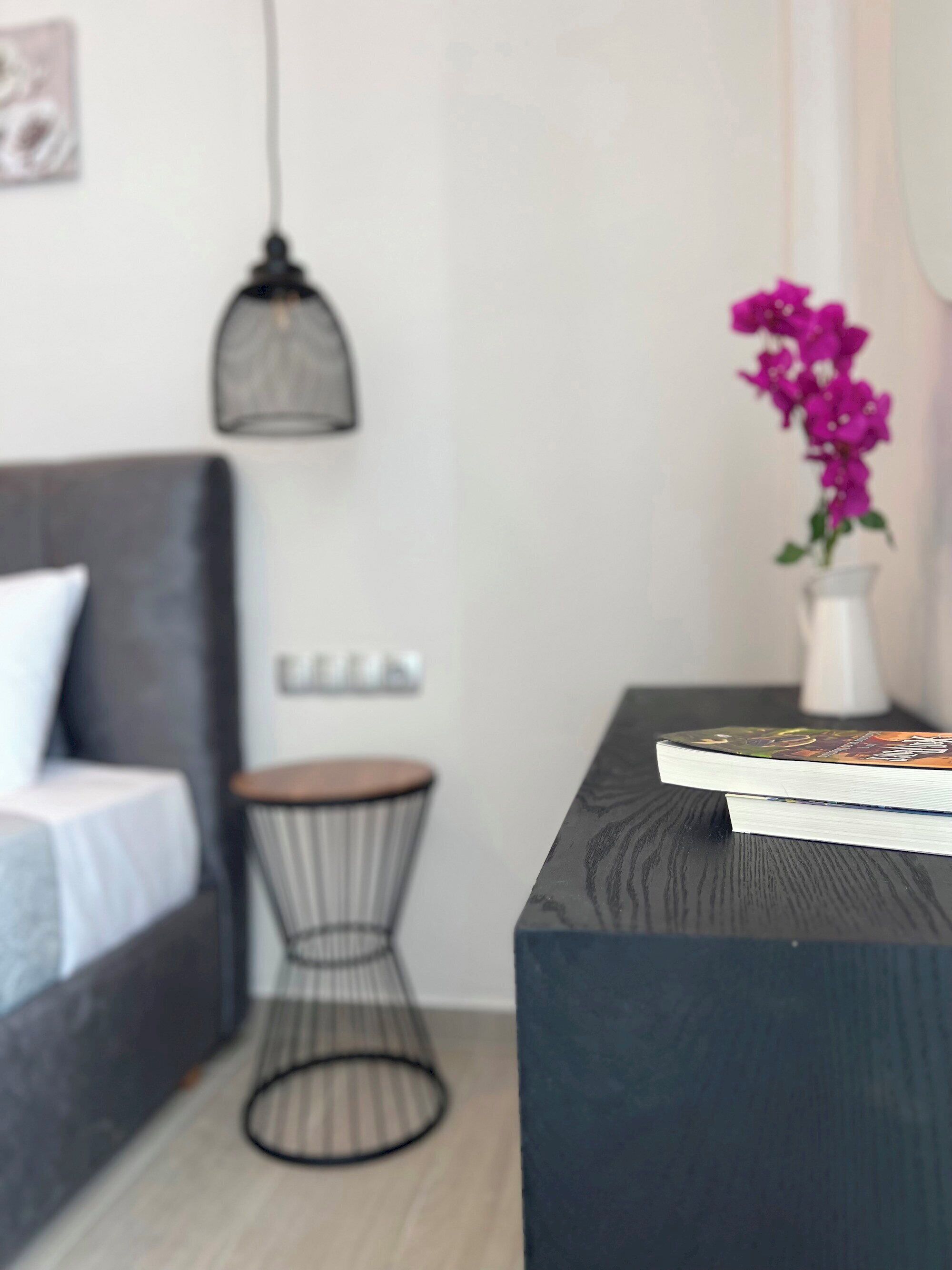 A modern living room with a dark sofa, a round side table, a hanging light fixture, and a vase with purple flowers.