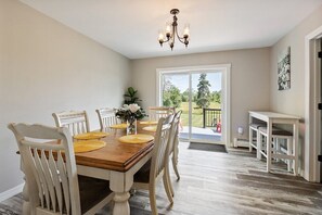 A dining area with a wooden table and chairs, a chandelier, and a view of the outdoors through a sliding glass door.