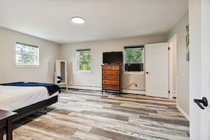 A bedroom with a bed, dresser, TV, and windows.