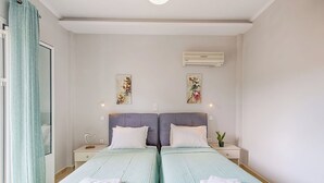 Quarto de hotel com duas camas, uma janela com cortinas, um aparelho de ar condicionado e dois quadros pendurados na parede.