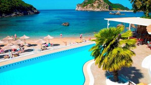 Zona junto a la piscina con vista al mar, sombrillas y sillones de descanso.