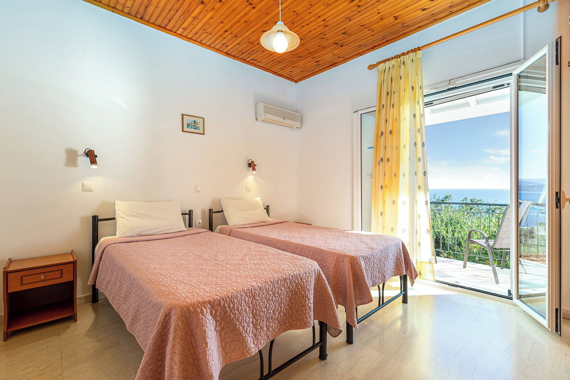 Une chambre avec deux lits, un plafond en bois, une fenêtre avec des rideaux et un balcon offrant une vue.