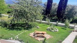 Ein gepflegter Garten mit einem Feuerkorb aus Holz, einem Pflasterweg und verschiedenen Pflanzen.