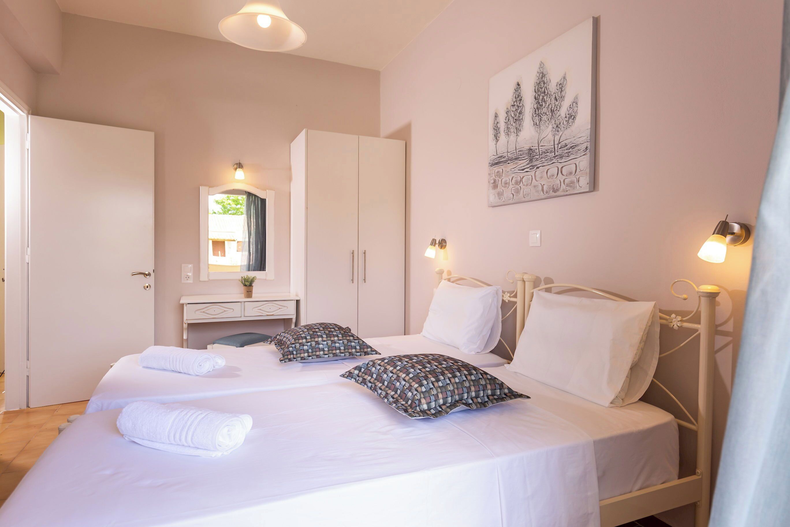 A bedroom with two beds, a wardrobe, a bedside table with a mirror, and wall-mounted lights.