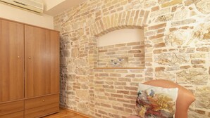 Una habitación con pared de piedra, armario de madera y una silla con cojín.