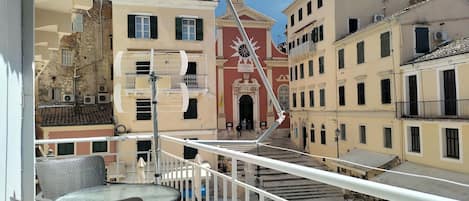 Un balcone con posti a sedere all'aperto, vista su un edificio storico dalla facciata rossa e un emblema solare bianco, e una scala che conduce all'ingresso dell'edificio.