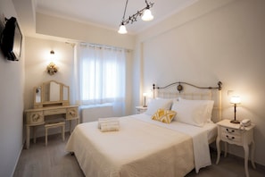 Quarto com cama, mesas de cabeceira, cômoda, espelho, janela com cortinas e um candelabro.
