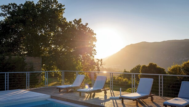 Zona de piscina con sillones reclinables y vistas a una cordillera.
