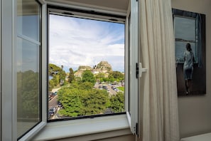 Une pièce dotée d’une grande fenêtre donnant sur un bâtiment historique et un parking.