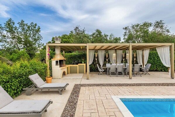 Un espace aménagé au bord de la piscine, avec des chaises longues, un coin salon abrité et un barbecue.