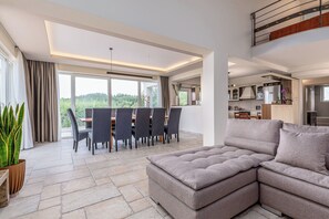 Un salon moderne avec un canapé d’angle, un coin repas avec des chaises et une cuisine en arrière-plan.
