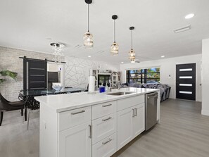 A modern kitchen with a central island, pendant lighting, and a view to the living area.