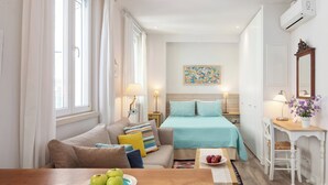 A room with a bed, a sofa, a dining table with apples, and a desk with a lamp and flowers. - Studio No2, CasaNova, Corfu old town center (Corfu)