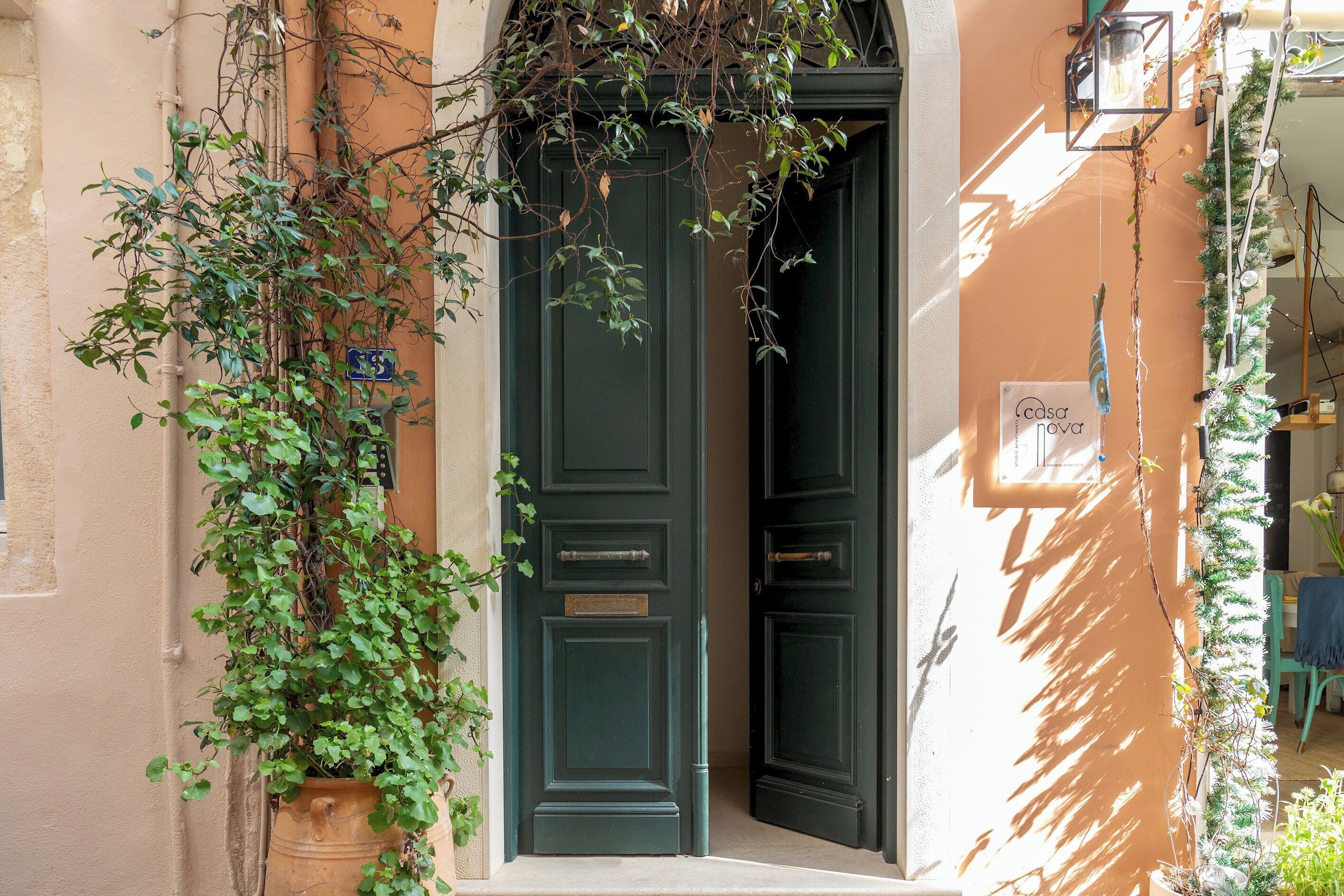 A building entrance with a green door, a potted plant, and a sign.