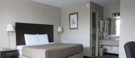 Une chambre d’hôtel avec un grand lit, des lampes de chevet, un petit bureau, une salle de bain avec un lavabo et un miroir, et un tableau encadré au mur.