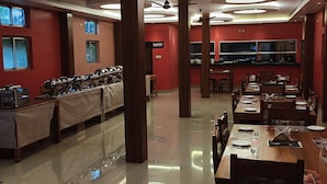 A spacious dining area with multiple tables and chairs, a visible kitchen area, and a sign indicating a pantry. - Lilawati's Blue Fox (Sonapur)