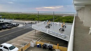 Eine Dachterrasse mit Blick auf Strand und Meer, ein Parkplatz sowie Außenmöbel.