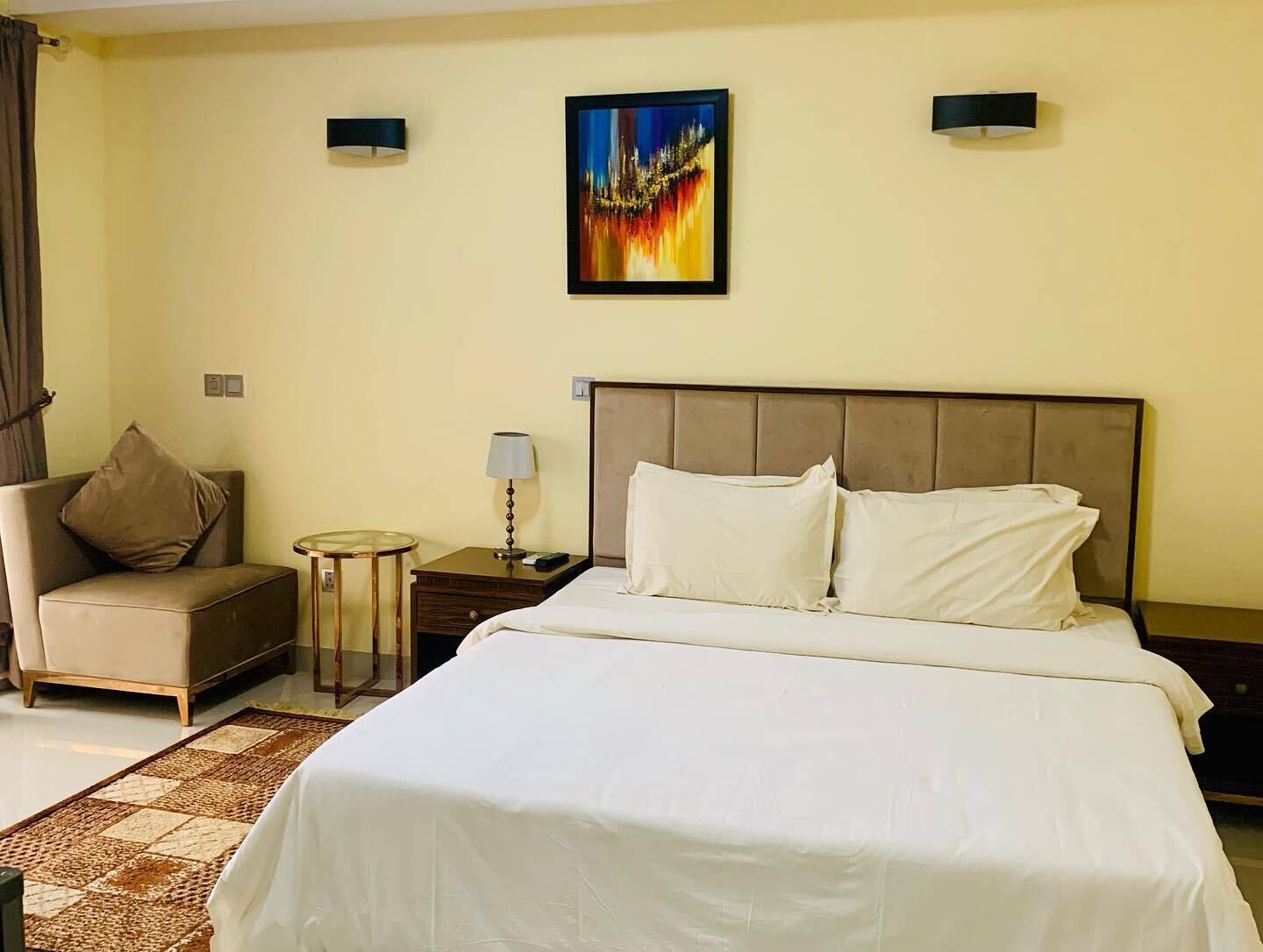 Une chambre d’hôtel avec un grand lit, une chaise, une petite table et un tableau au mur.