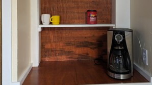 Een keukenschap met mokken, een koffiezetapparaat en een Folgers koffiebus.