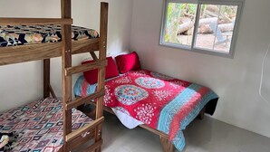 Une chambre avec un lit superposé, une fenêtre et une vue sur les troncs d’arbres à l’extérieur.