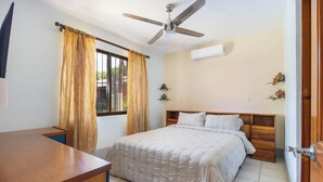 A bedroom with a bed, a desk, a ceiling fan, and a window with curtains. - Las Palmas Condo: Pool & Beach (Coco)