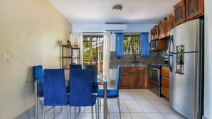 A modern kitchen with a dining area, featuring a stainless steel refrigerator, wooden cabinets, and blue chairs. - Las Palmas Condo: Pool & Beach (Coco)