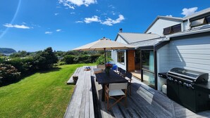 En træterrasse med et bord, stole, grill og stor parasol.