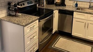 Una cocina con armarios blancos, estufa de acero inoxidable, microondas, tostadora y cafetera.