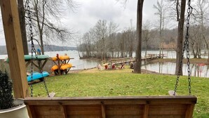 Un conjunto de columpios de madera con vista a un lago, con sillas y un pequeño muelle.
