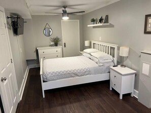 Un dormitorio con cama, mesitas de noche, ventilador de techo, espejo y estante con adornos.