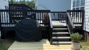 Ein Garten mit einer Holzterrasse, einem Grill, Gartenmöbeln und einem Blumentopf.