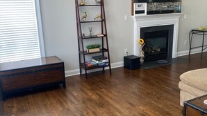 Ein Wohnzimmer mit Holzdielen, einem Kamin, einem darüber montierten Fernseher und einem Hängeregal mit Dekoration.