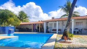 Una piscina con bordo piastrellato, un patio coperto con posti a sedere e una palma.