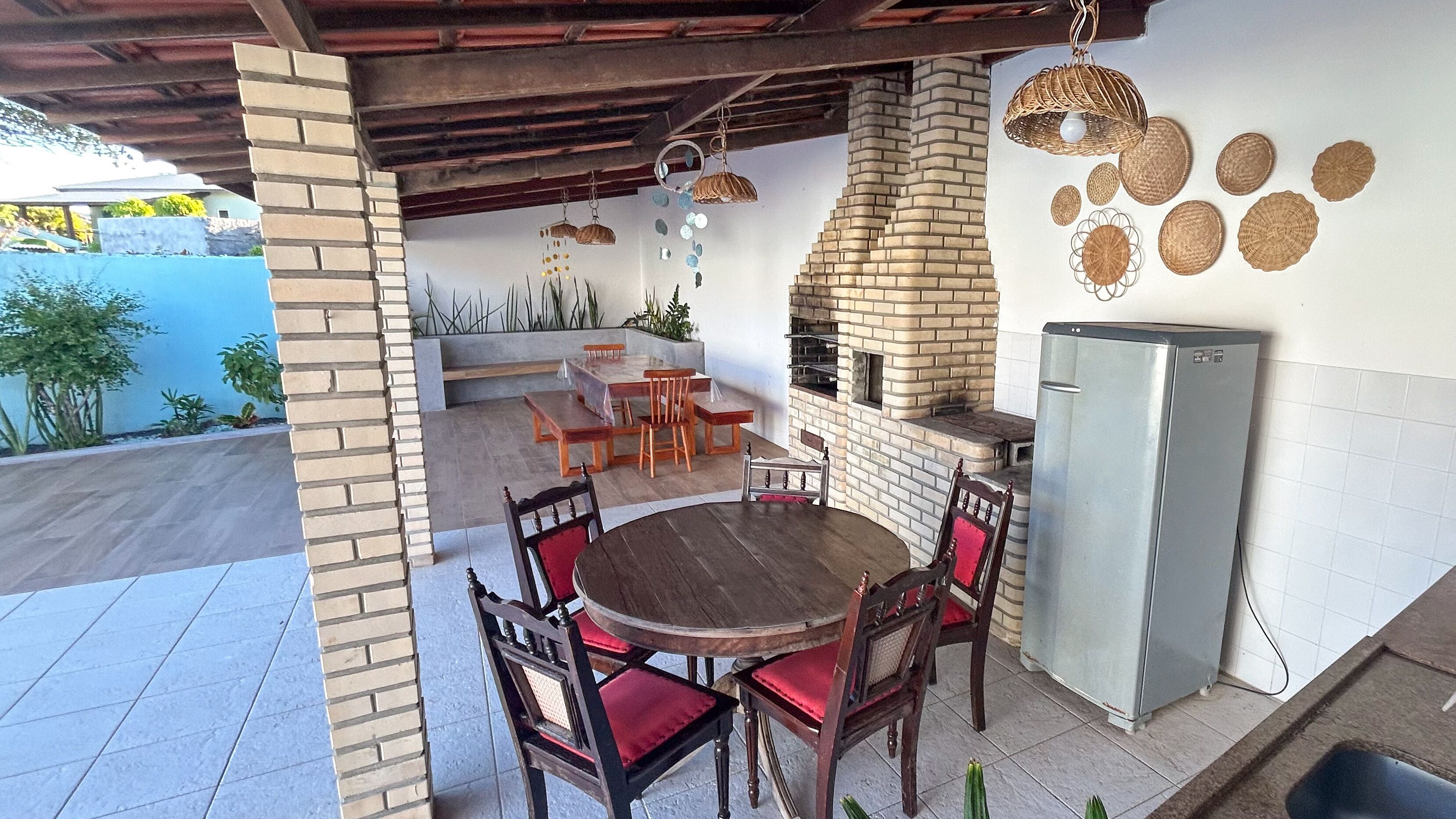 An outdoor patio with a brick fireplace, a dining table with chairs, and a refrigerator.