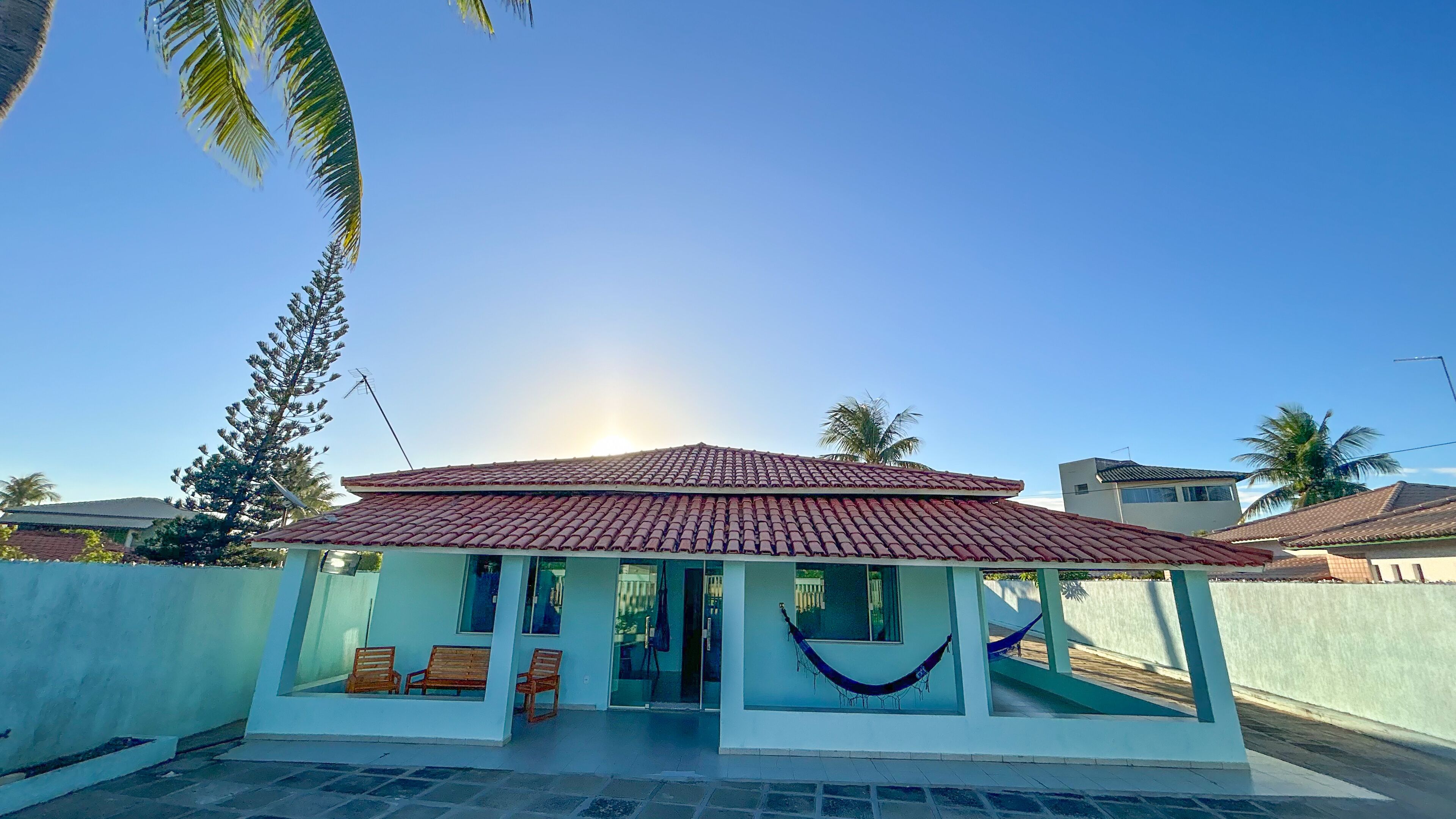 A small, single-story building with a tiled roof, a porch with benches, and a hammock.