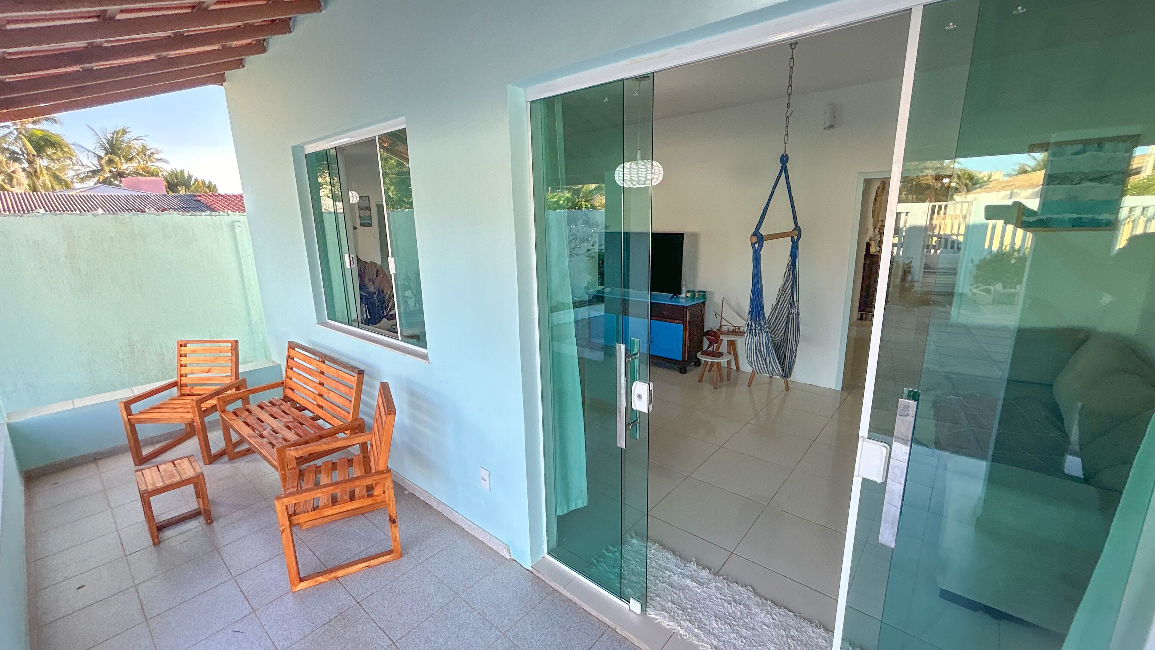A room with a glass door leading to a balcony, a wooden bench, and a hanging chair.