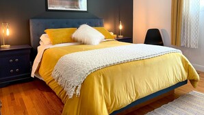 Un dormitorio moderno con una cama, dos mesitas de noche, una silla y una obra de arte en la pared.