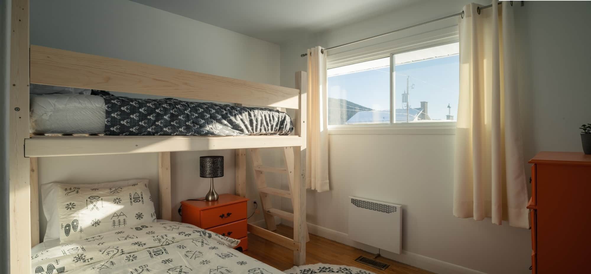 Habitación con literas, ventana, calentador, mesita de noche y cómoda.