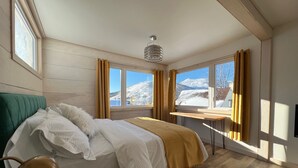A bedroom with a bed, a desk, and a view of a snowy landscape through large windows.