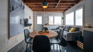 Una cocina moderna con techo de madera, una mesa redonda con sillas, un sofá gris con cojines y un amplio ventanal que proporciona luz natural.