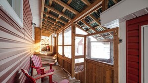 Une terrasse en bois avec des fauteuils Adirondack rouges, une porte vitrée et une vue sur un paysage enneigé.