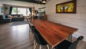 Une cuisine moderne avec une table à manger en bois, des chaises noires, des luminaires suspendus et un grand tableau accroché au mur.
