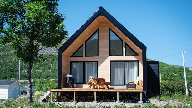 Una cabaña moderna con fachada de madera, ventanas amplias y una terraza.