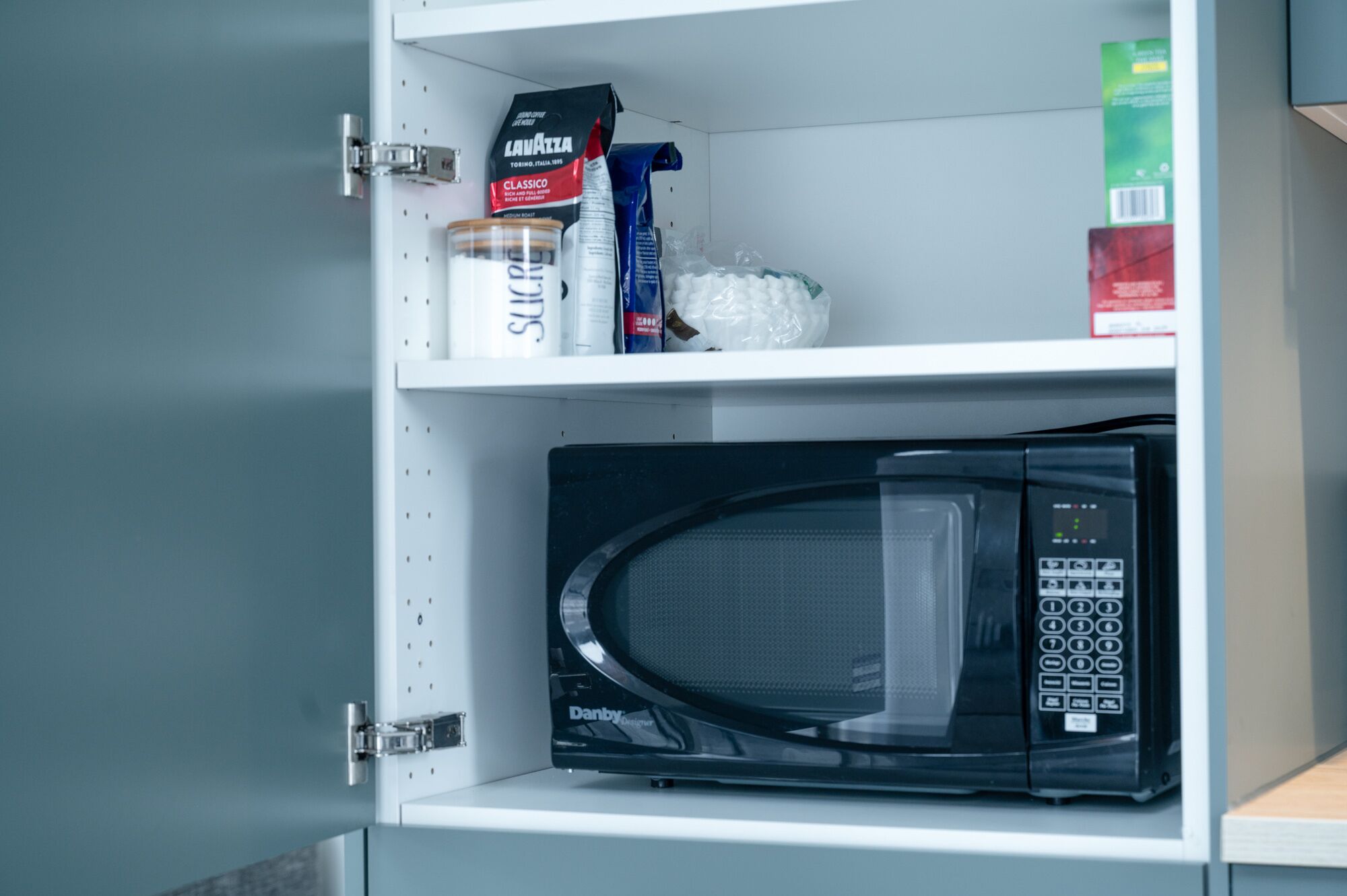 A kitchen cabinet with a microwave and various food items.